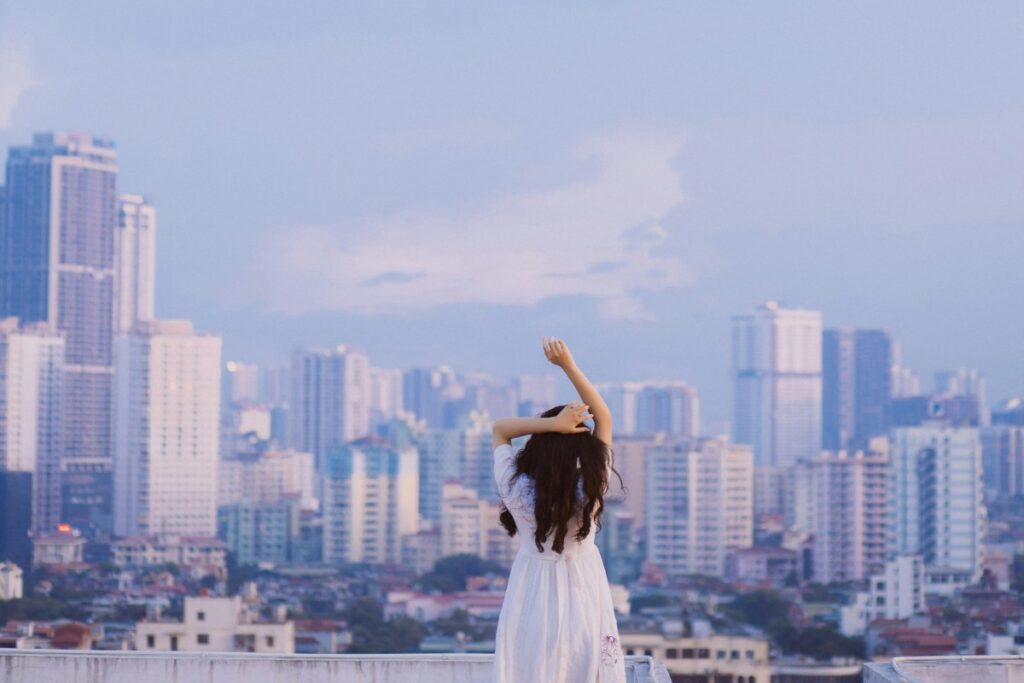 Cảnh ảnh một cô gái với mái tóc dài, mặc chiếc váy trắng tinh khôi, đứng trên mái nhà cao tầng, tay chống nạnh, enjoying the gentle breeze and the beautiful cityscape before her. Giới Thiệu Về BaoLiba – Cách Mạng Hợp Tác Giữa Thương Hiệu & Người Ảnh Hưởng tại Việt Nam, nơi kết nối những thương hiệu với người ảnh hưởng một cách minh bạch và hiệu quả.
